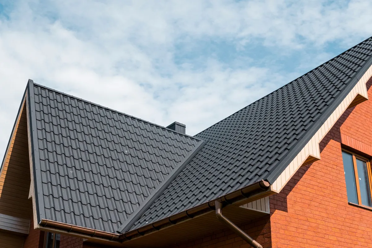 Modern dark metal roof on a brick house against a blue sky
