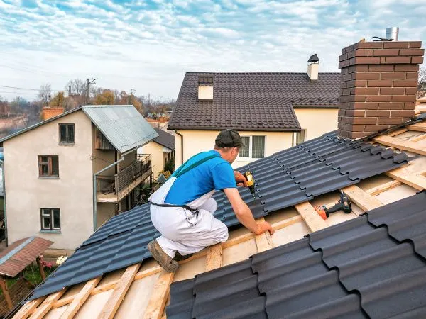 Roofer installing dark metal roof panels on a residential roof