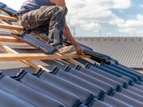 Roofer installing dark roof tiles over wooden battens
