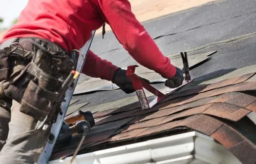 Roofer removing old shingles with a pry bar during a repair