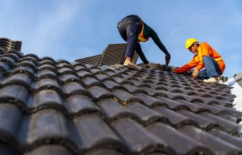 Roofing crew installing dark shingle tiles on a residential roof