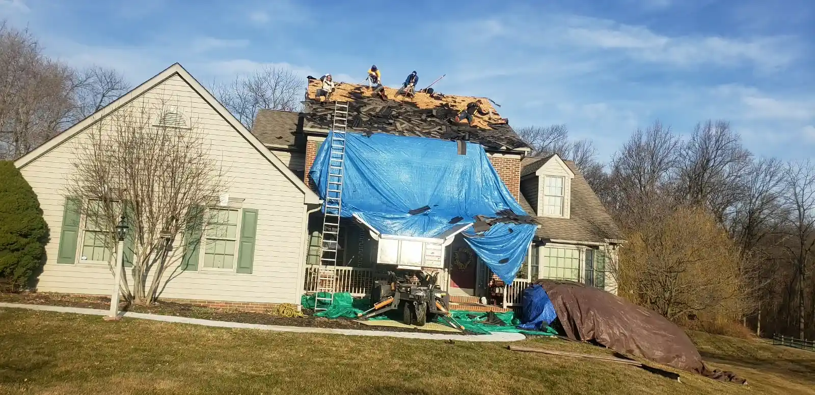 Roofing crew replacing a roof covered with a blue protective tarp