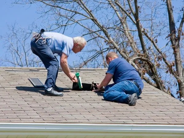 Two roofers repairing a shingle roof with hand tools