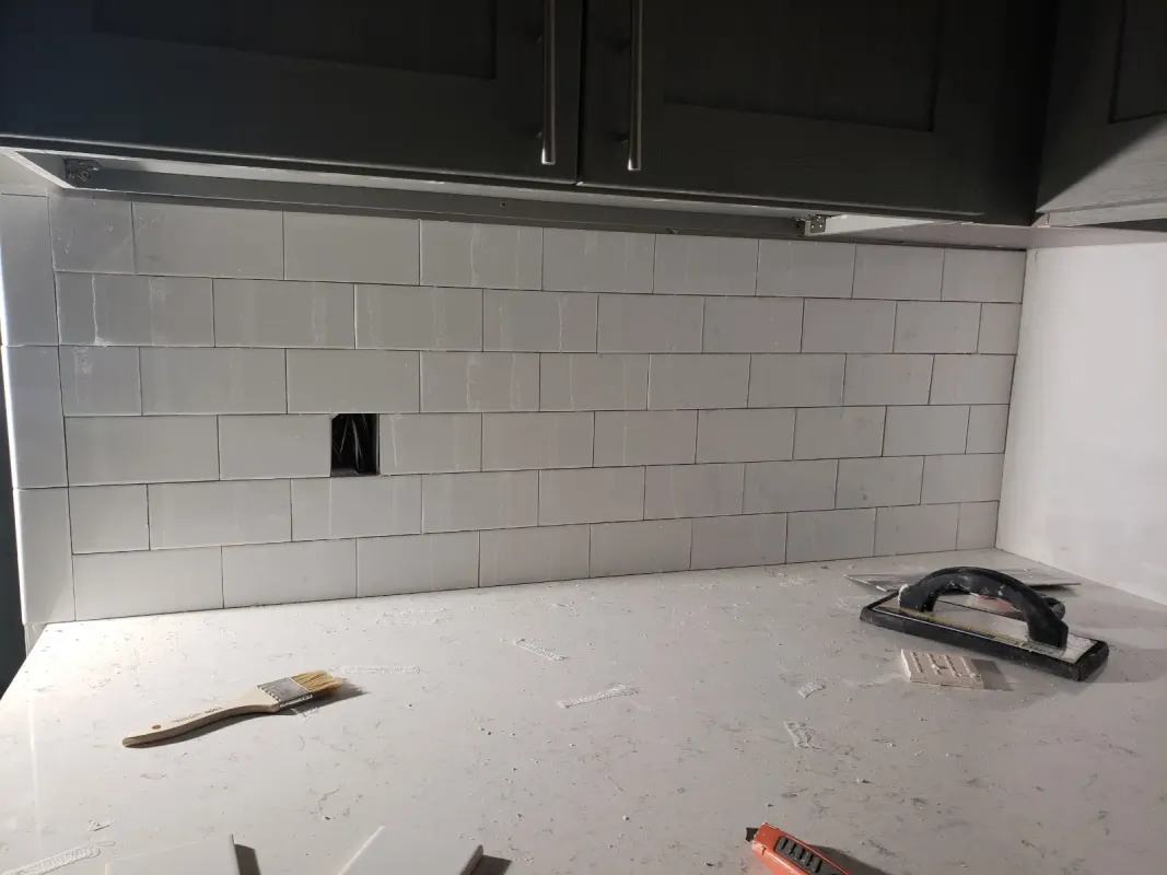 White subway tile kitchen backsplash installation in progress with tools