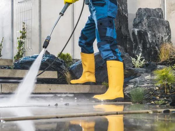 Worker power washing a stone patio with a pressure washer