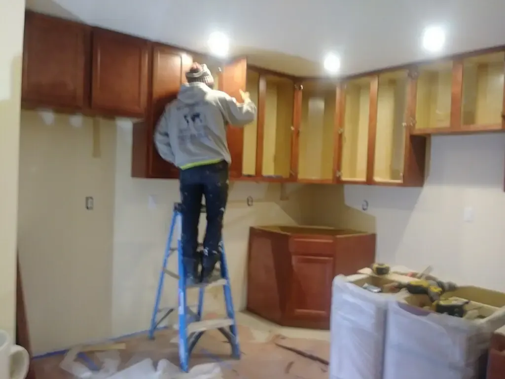 Worker on a stepladder installing wooden kitchen cabinets during a remodel